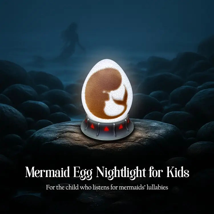 OstanesKids mermaid egg nightlight glowing on a rocky shore, with red gem base and a distant silhouette of a mermaid.